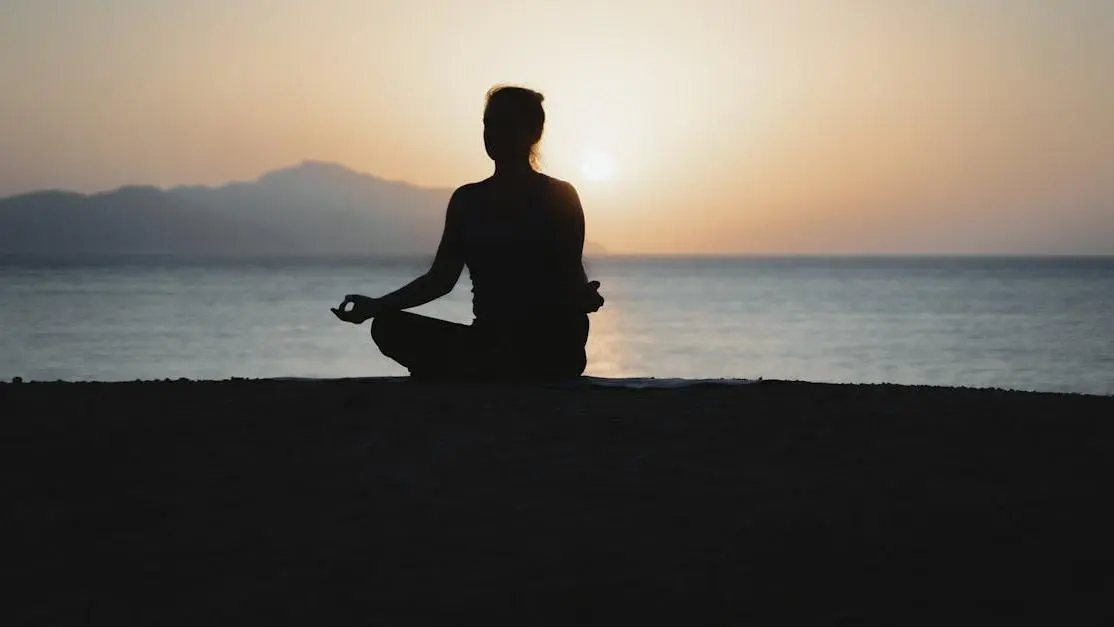 Woman doing evening yoga for sleep by the ocean at sunset, promoting relaxation and calm.