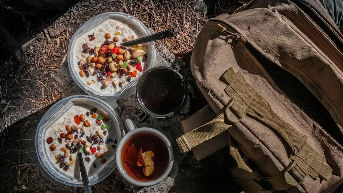 Assorted healthy snacks for travel, including fruit and nuts, arranged outdoors with a backpack.