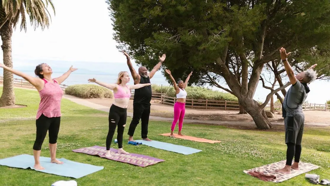 Diverse group practicing hip opener yoga poses outdoors in a sunny park setting